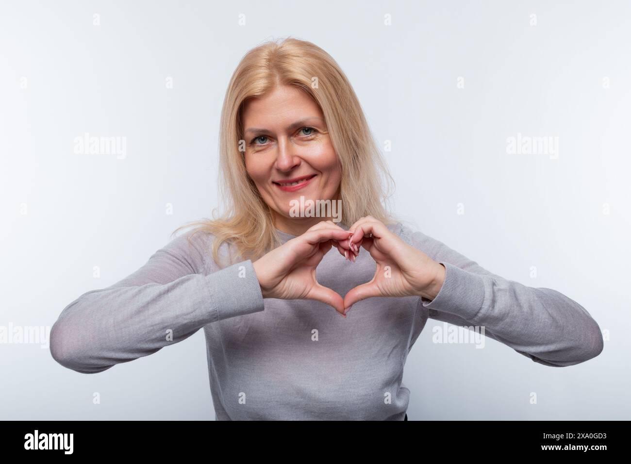 Charmante femme de 45 ans avec les cheveux blonds montre le geste du cœur Banque D'Images