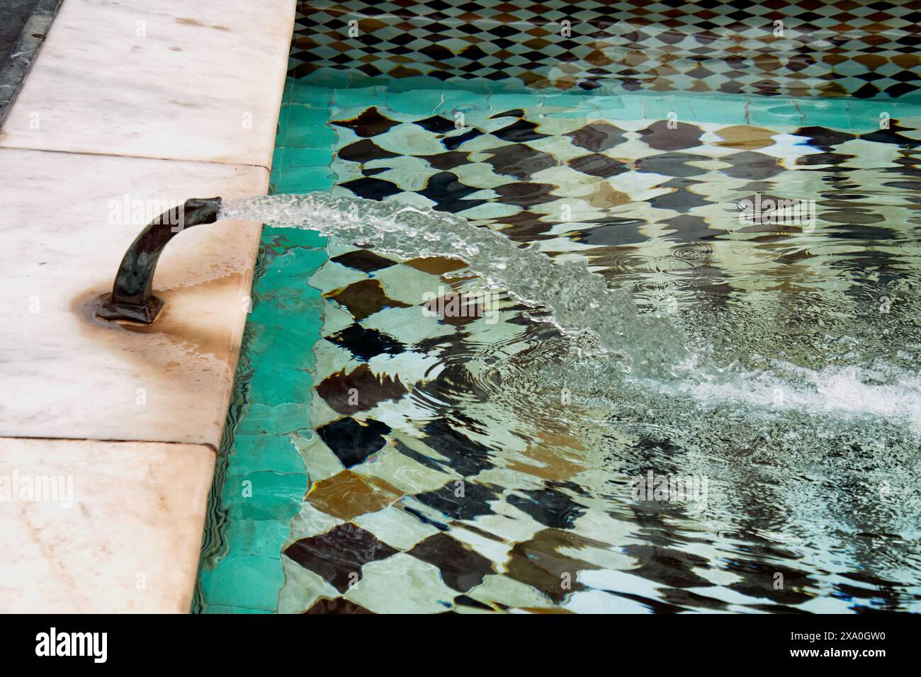 Une fontaine marocaine à la Madrasa Ben Youssef à Marrakech recouverte de petits carreaux colorés et d’un robinet en bronze libérant de l’eau Banque D'Images