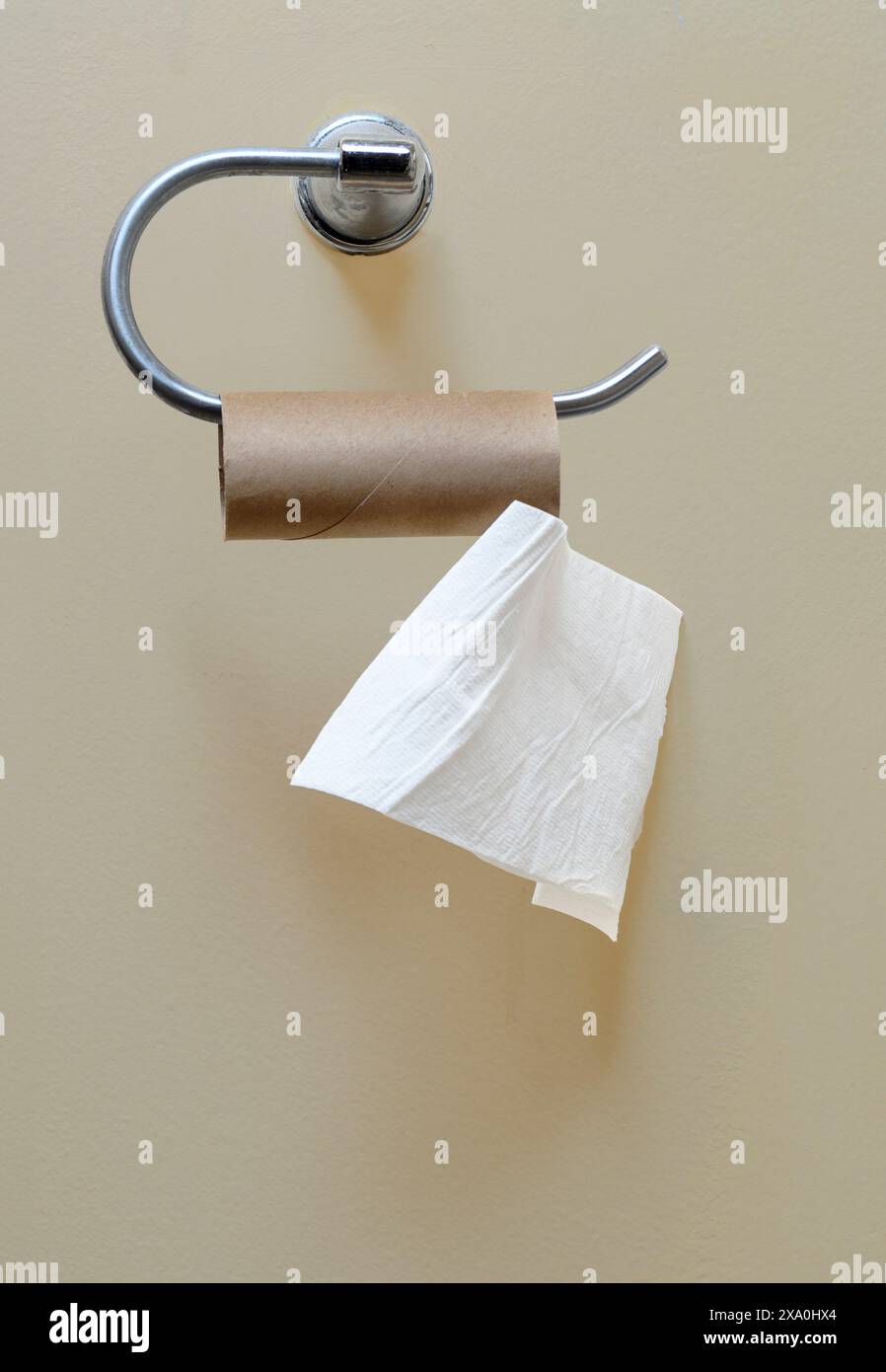 Plan vertical d'un rouleau de papier toilette presque vide suspendu au support de papier toilette sur le mur de la salle de bain. Banque D'Images