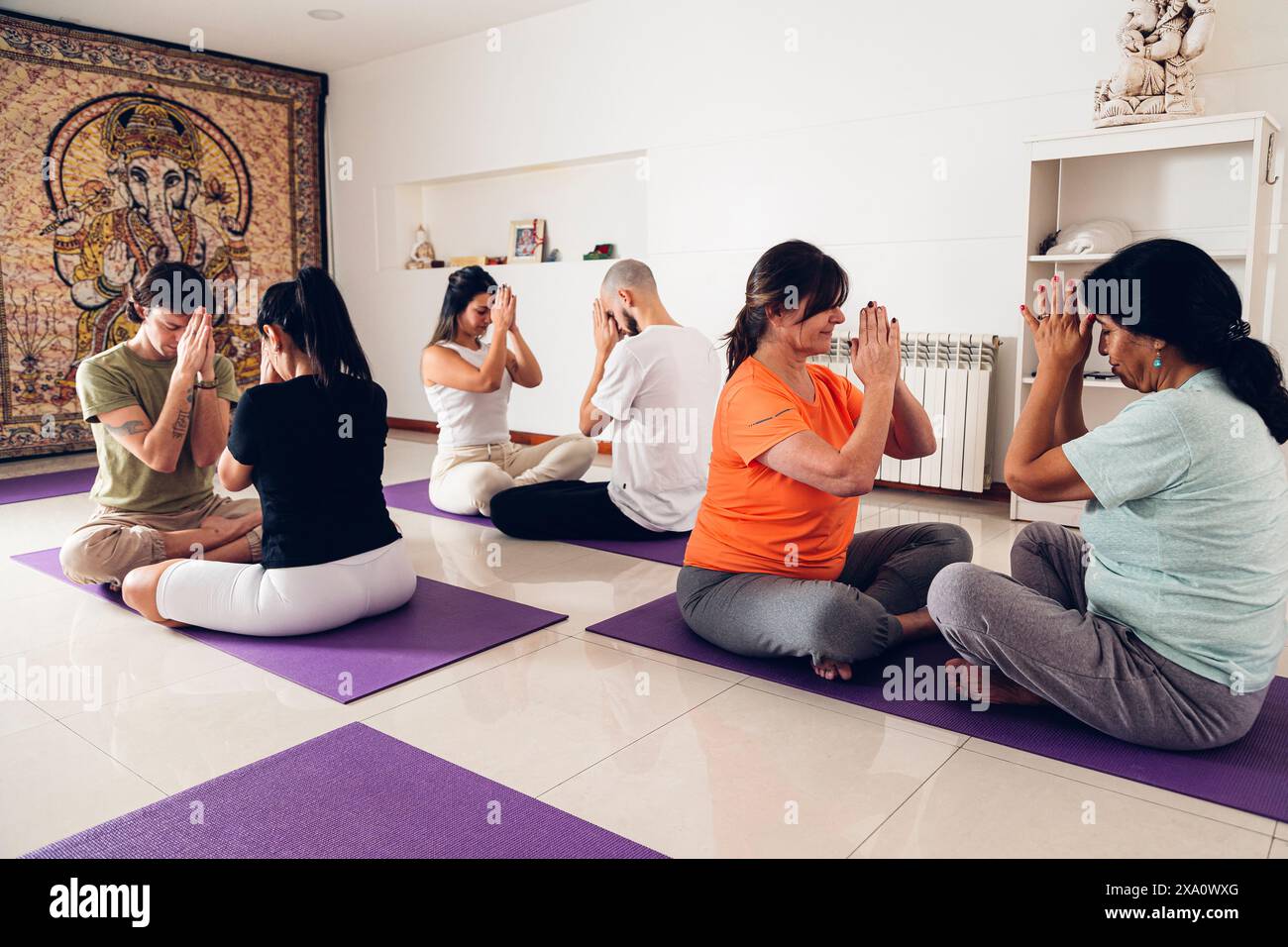 Les gens dans un cours de yoga. Ils font la position de prière avec leurs mains levées tout en étant assis sur un tapis dans le gymnase. Banque D'Images