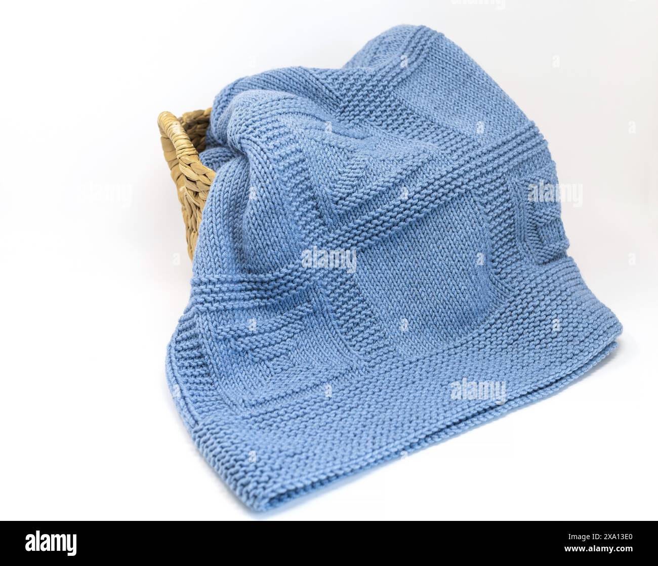 photographie d'une couverture tricotée à la main en laine bleue texturée en motif de tricotage géométrique dans un panier isolé sur un fond blanc Banque D'Images