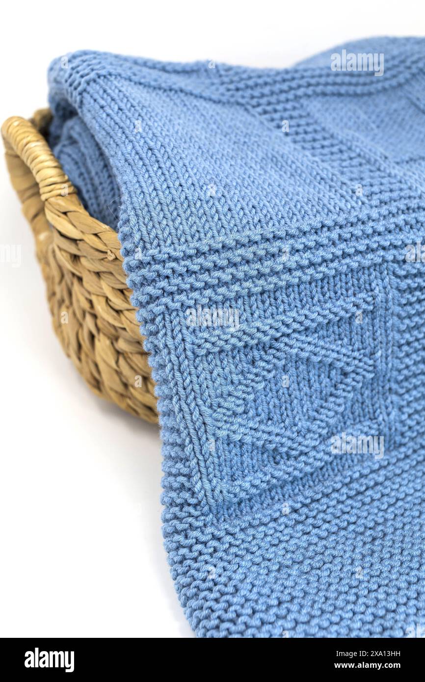 Photographie rapprochée d'une couverture tricotée à la main texturée en laine bleue dans un motif de tricot géométrique dans un panier sur un fond blanc Banque D'Images
