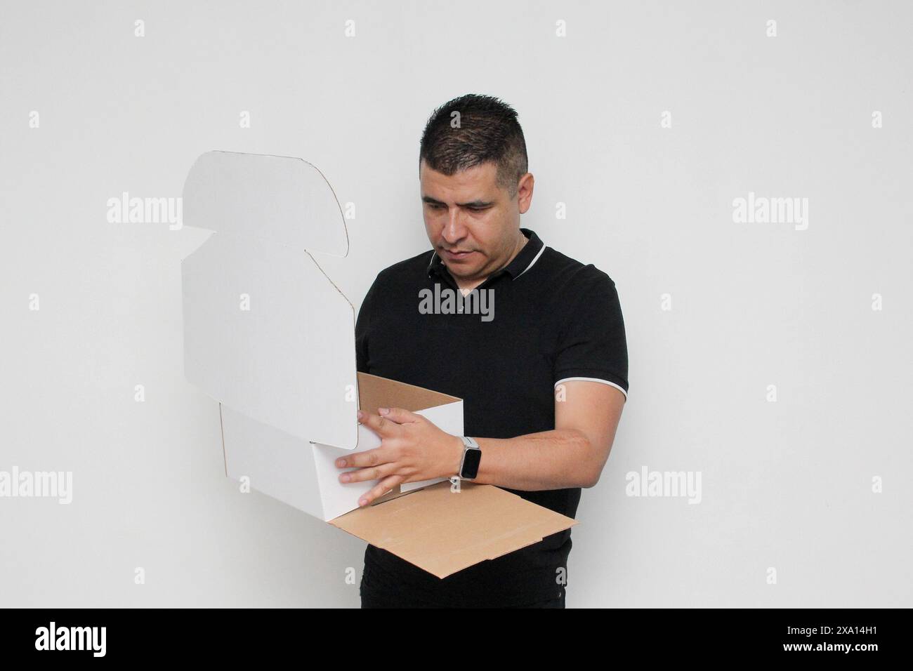 Homme adulte Latino à peau foncée assemble une boîte en carton suivant les instructions concentrée et attentive Banque D'Images Homme adulte Latino à peau foncée assemble une boîte en carton suivant les instructions concentrée et attentive Banque D'Images
