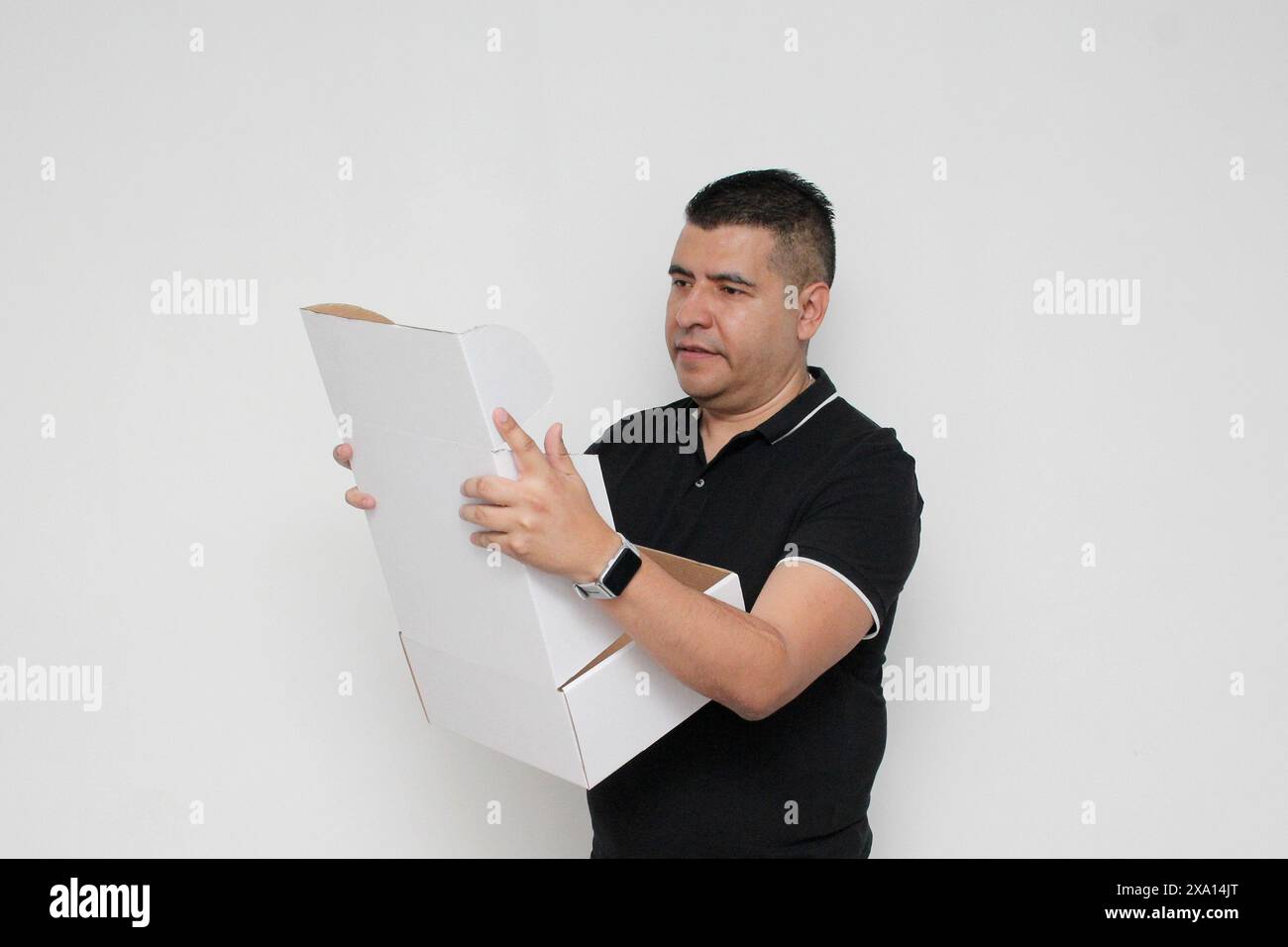 Homme adulte Latino à peau foncée assemble une boîte en carton suivant les instructions concentrée et attentive Banque D'Images Homme adulte Latino à peau foncée assemble une boîte en carton suivant les instructions concentrée et attentive Banque D'Images