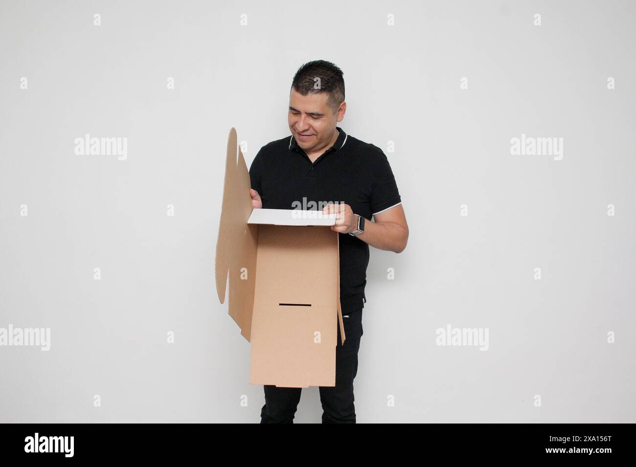 Homme adulte Latino à peau foncée assemble une boîte en carton suivant les instructions concentrée et attentive Banque D'Images Homme adulte Latino à peau foncée assemble une boîte en carton suivant les instructions concentrée et attentive Banque D'Images