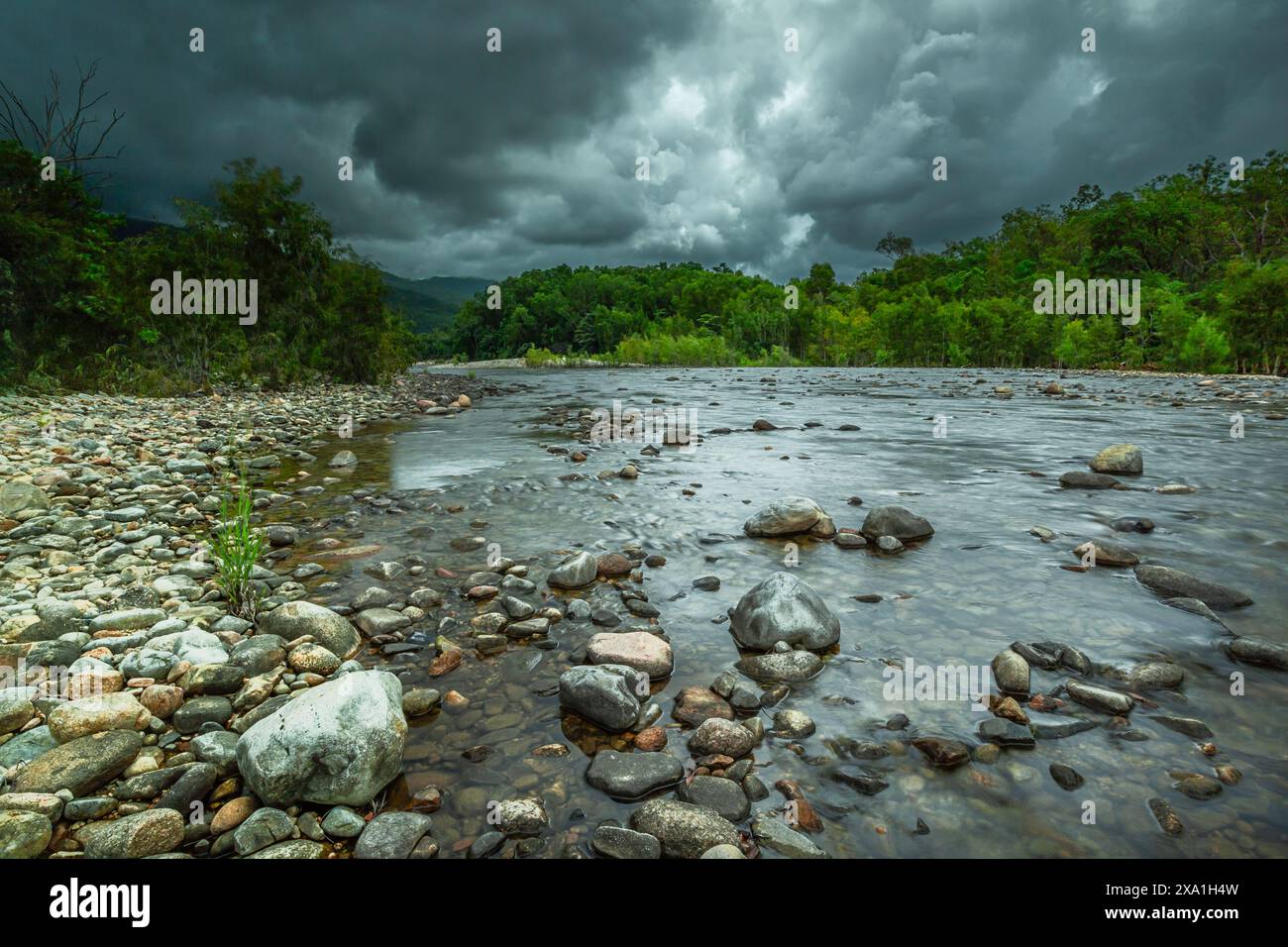 Rivage rocheux par l'eau sous les nuages de tempête imminents au sommet de la colline Banque D'Images