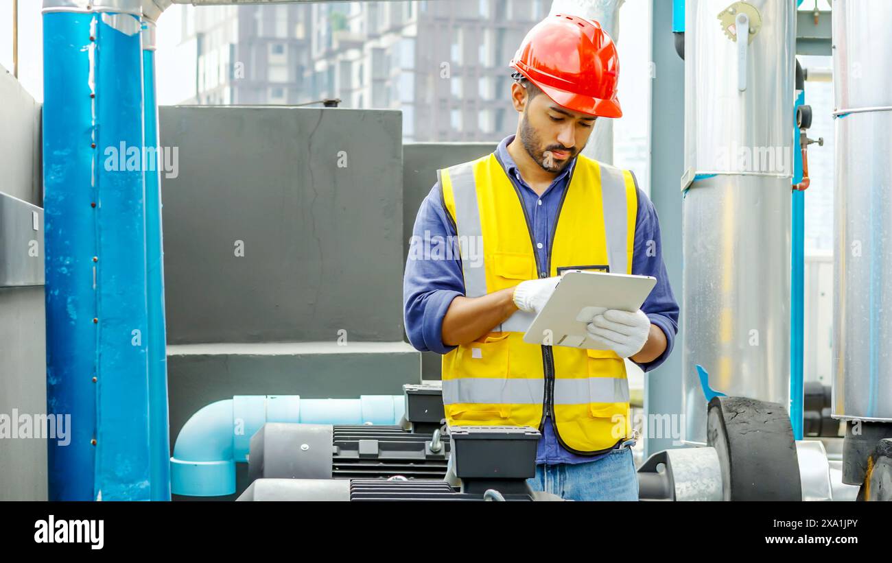 Un homme avec une tablette devant des tuyaux industriels. Banque D'Images
