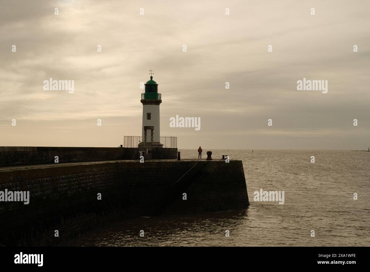Un phare sur la jetée avec des gens et des nuages Banque D'Images