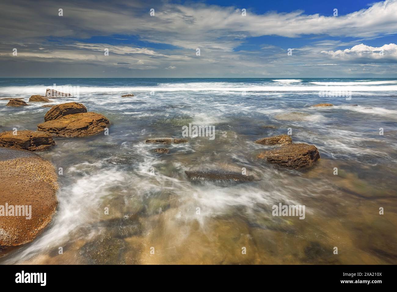 Les vagues de l'océan s'écrasent contre de nombreuses pierres dans une mer bleue vibrante à Moffat Beach, Queensland Banque D'Images