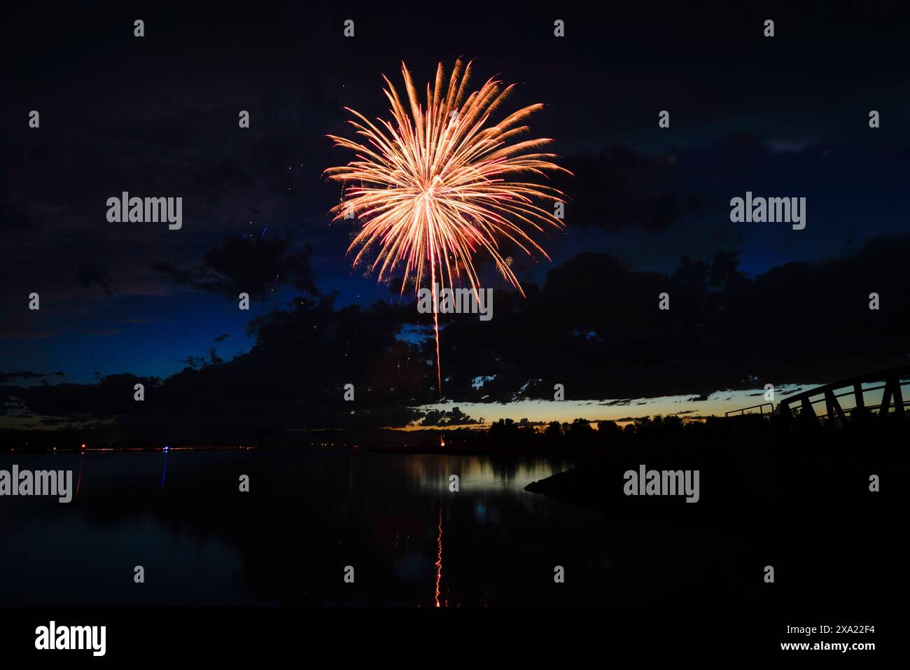 Des feux d'artifice colorés illuminent le ciel nocturne près d'un lac tranquille, créant un spectacle éblouissant de lumières Banque D'Images