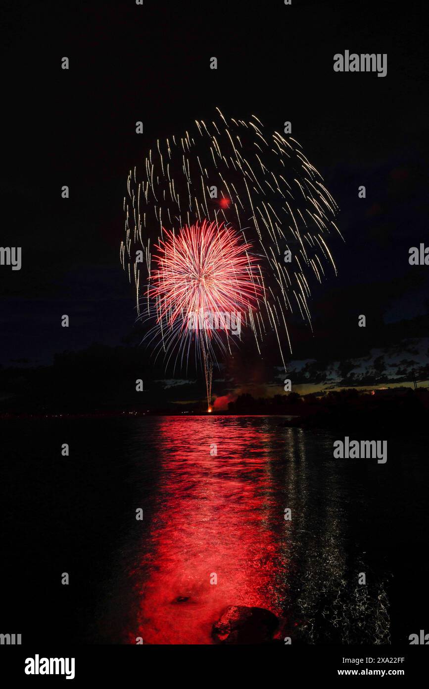 Photo nocturne de feux d'artifice éclairant le ciel au-dessus d'un lac et de montagnes Banque D'Images