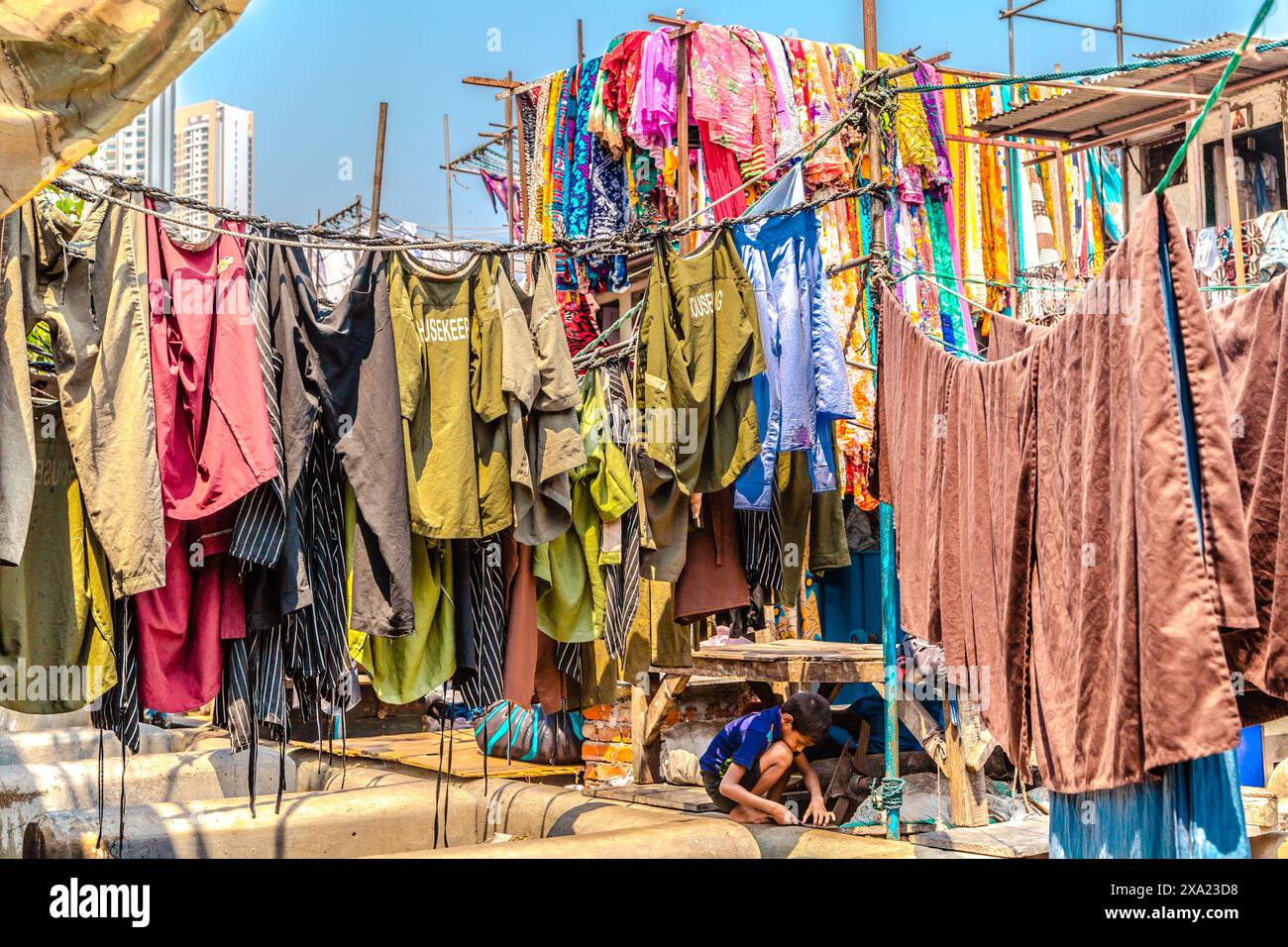 Un enfant jouant sous des vêtements suspendus vibrants à l'extérieur par une journée ensoleillée à Mumbai, en Inde Banque D'Images
