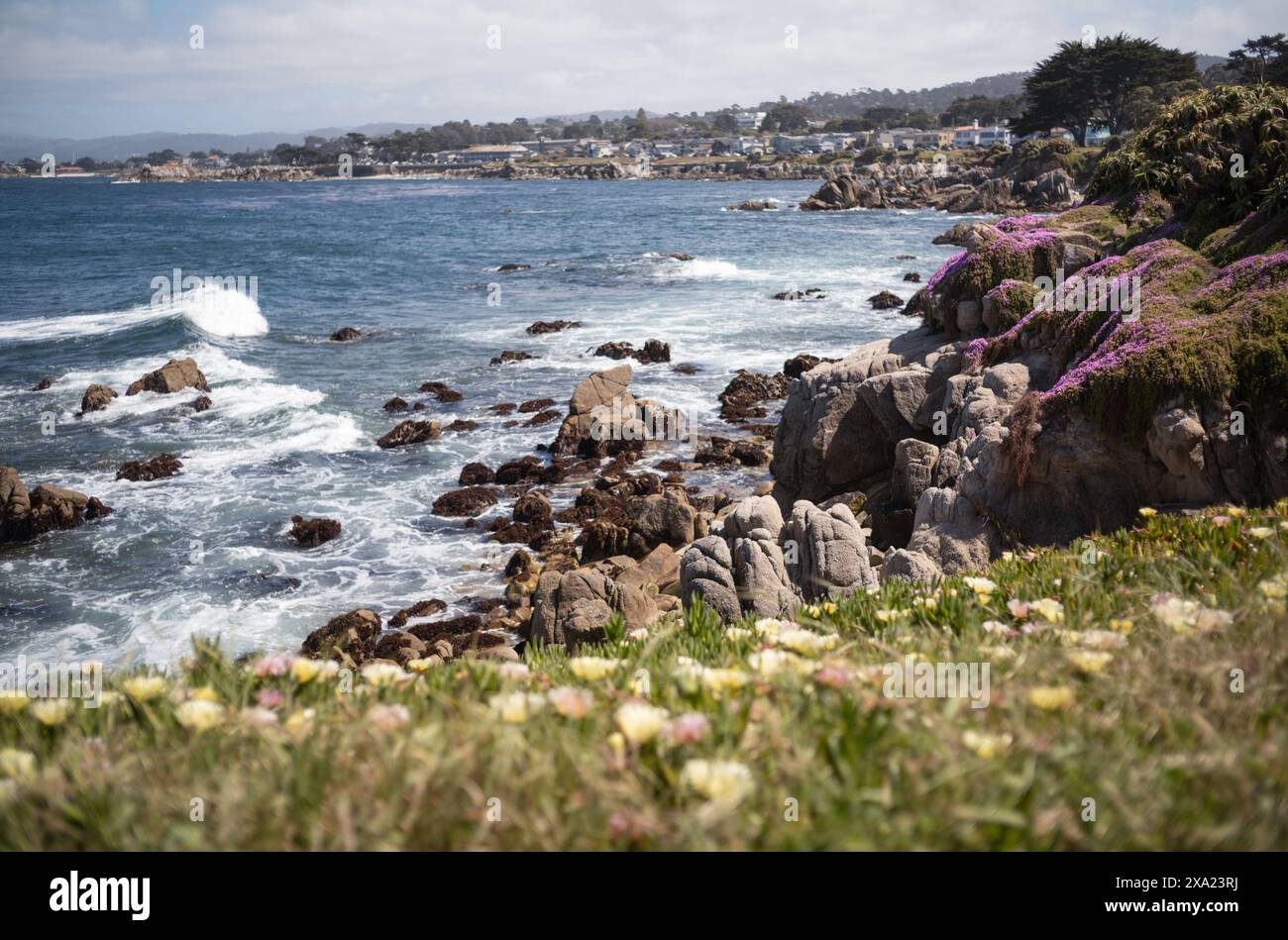 Les vagues de l'océan se brisent contre les rochers côtiers près d'un village balnéaire Banque D'Images