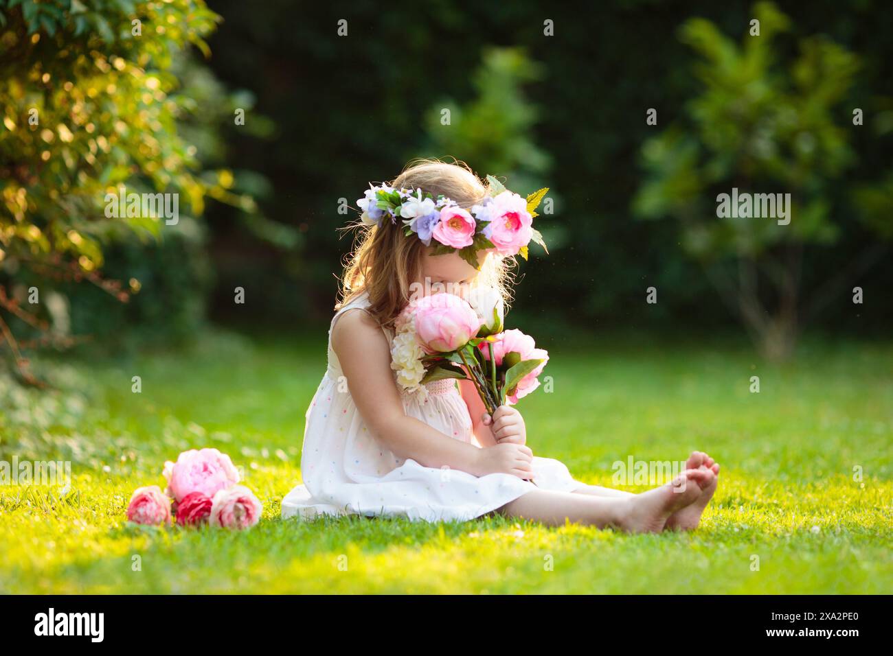 Petite fille avec bouquet de fleurs dans le jardin ensoleillé. Parc fleuri d'été. Enfant tenant le cadeau floral pour la fête d'anniversaire ou la célébration de Pâques. Banque D'Images