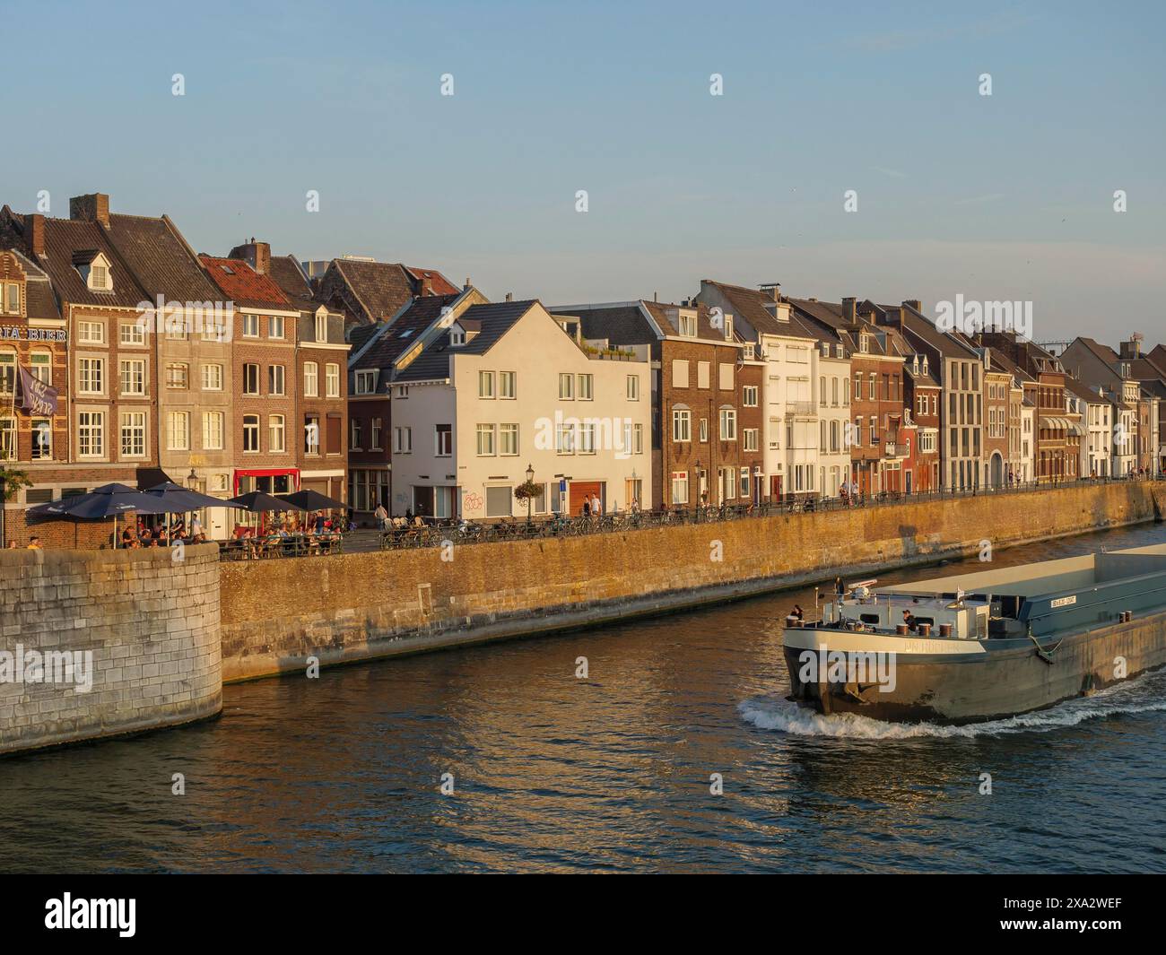 Grand navire naviguant le long d'une rangée de maisons sur une rive, Maastricht, pays-Bas Banque D'Images