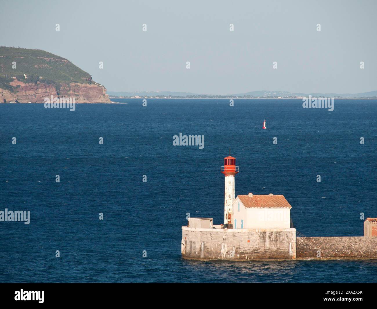 Phare blanc et rouge sur un mur dans la mer avec une île lointaine et un ciel bleu, la seyne sur mer, france Banque D'Images