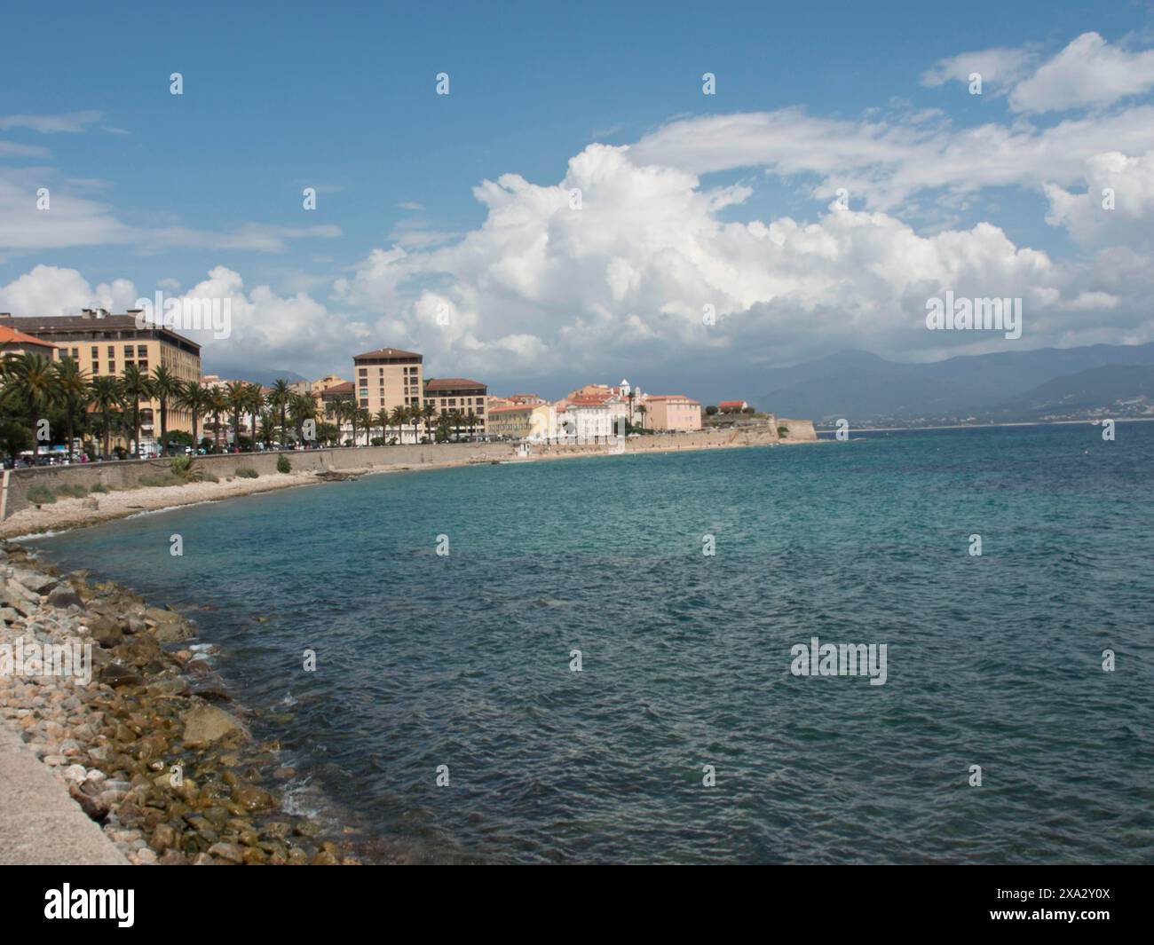 Ville côtière avec promenade et bâtiments le long d'une mer bleue claire sous un ciel nuageux, Corse, ajaccio, France Banque D'Images