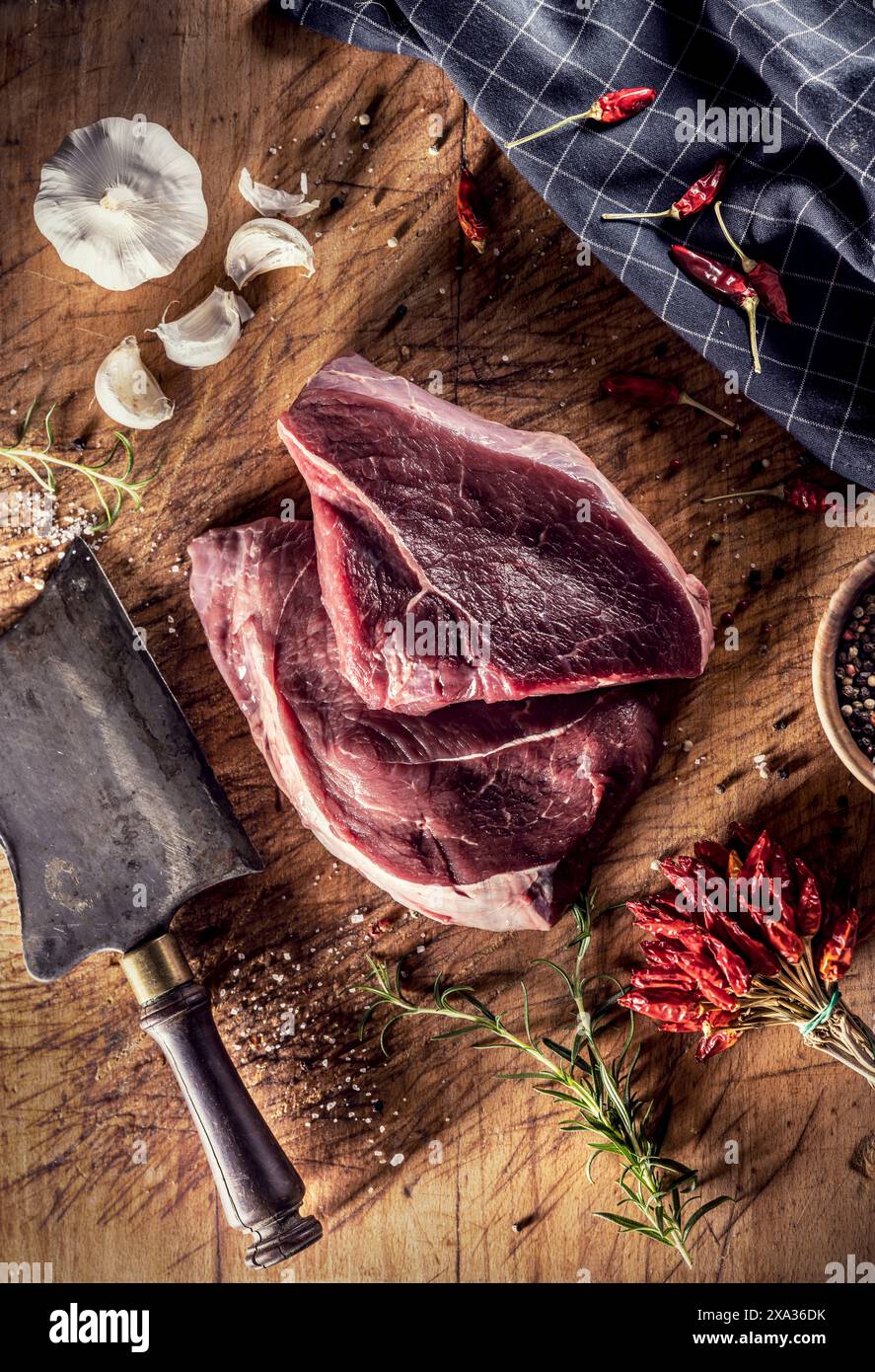 Deux steaks de bœuf sur une planche de boucherie, entourés d'épices, d'herbes et d'ail Banque D'Images