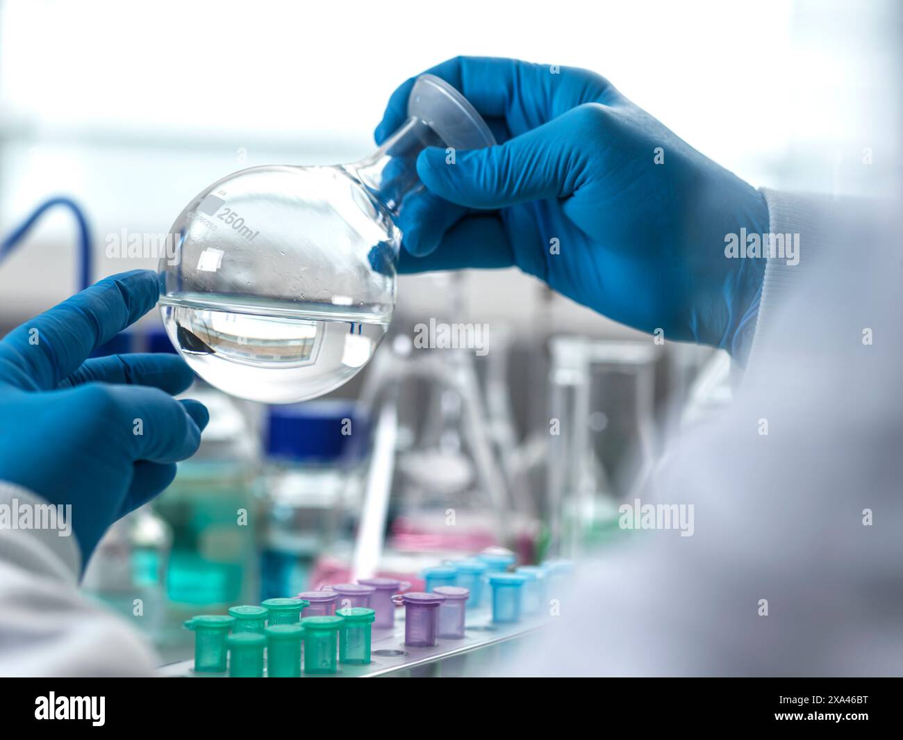 Mains gantées manipulant un flacon rond de laboratoire. Banque D'Images