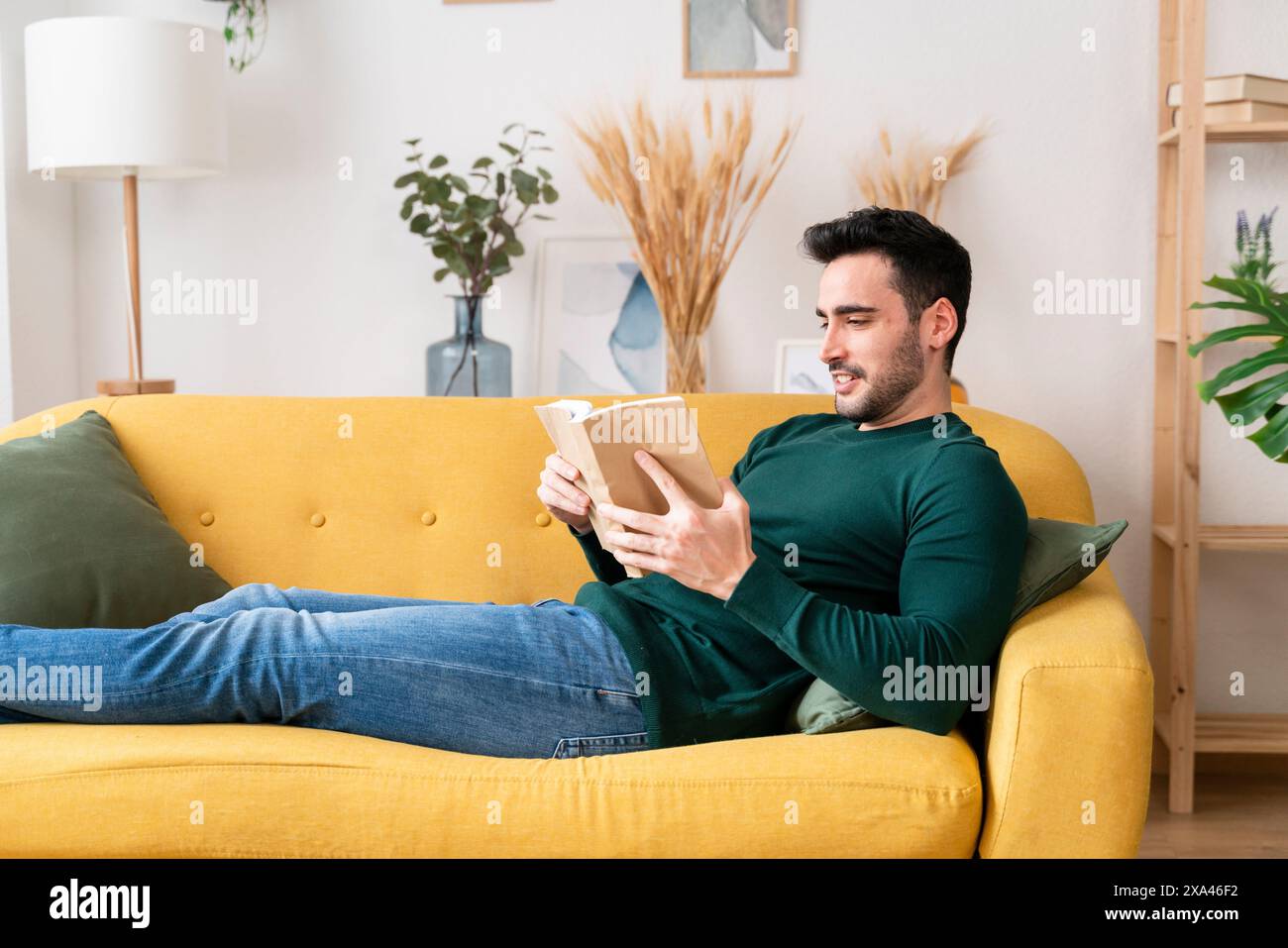 Homme lisant un livre sur un canapé jaune. Banque D'Images