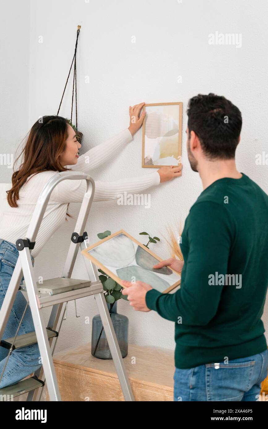 Couple accrochant un cadre photo sur un mur blanc Banque D'Images
