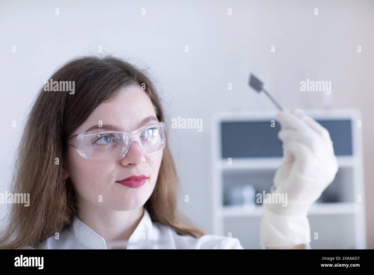 Une femme portant des lunettes de laboratoire examine attentivement un échantillon sur une lame de verre. Banque D'Images