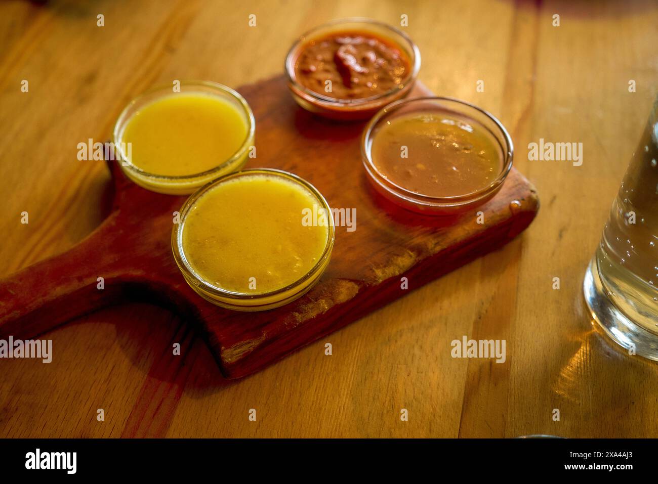 Une planche de service en bois avec trois petits bols de sauce et un pot de sauce sur une table en bois. Banque D'Images Une planche de service en bois avec trois petits bols de sauce et un pot de sauce sur une table en bois. Banque D'Images