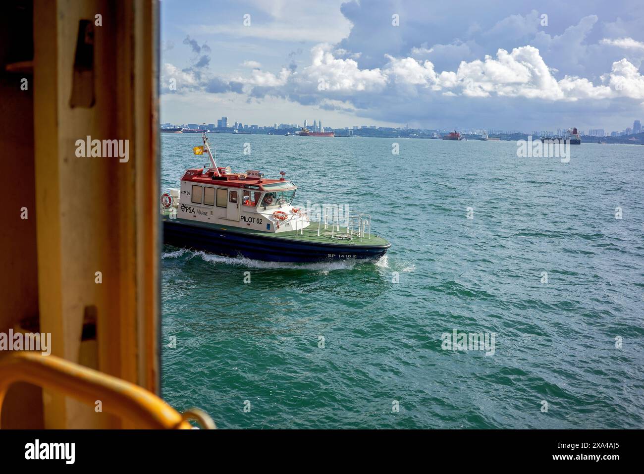 Un bateau-pilote navigue à travers une étendue d'eau, avec une ligne d'horizon de la ville au loin, observée du point de vue d'un navire plus grand. Banque D'Images