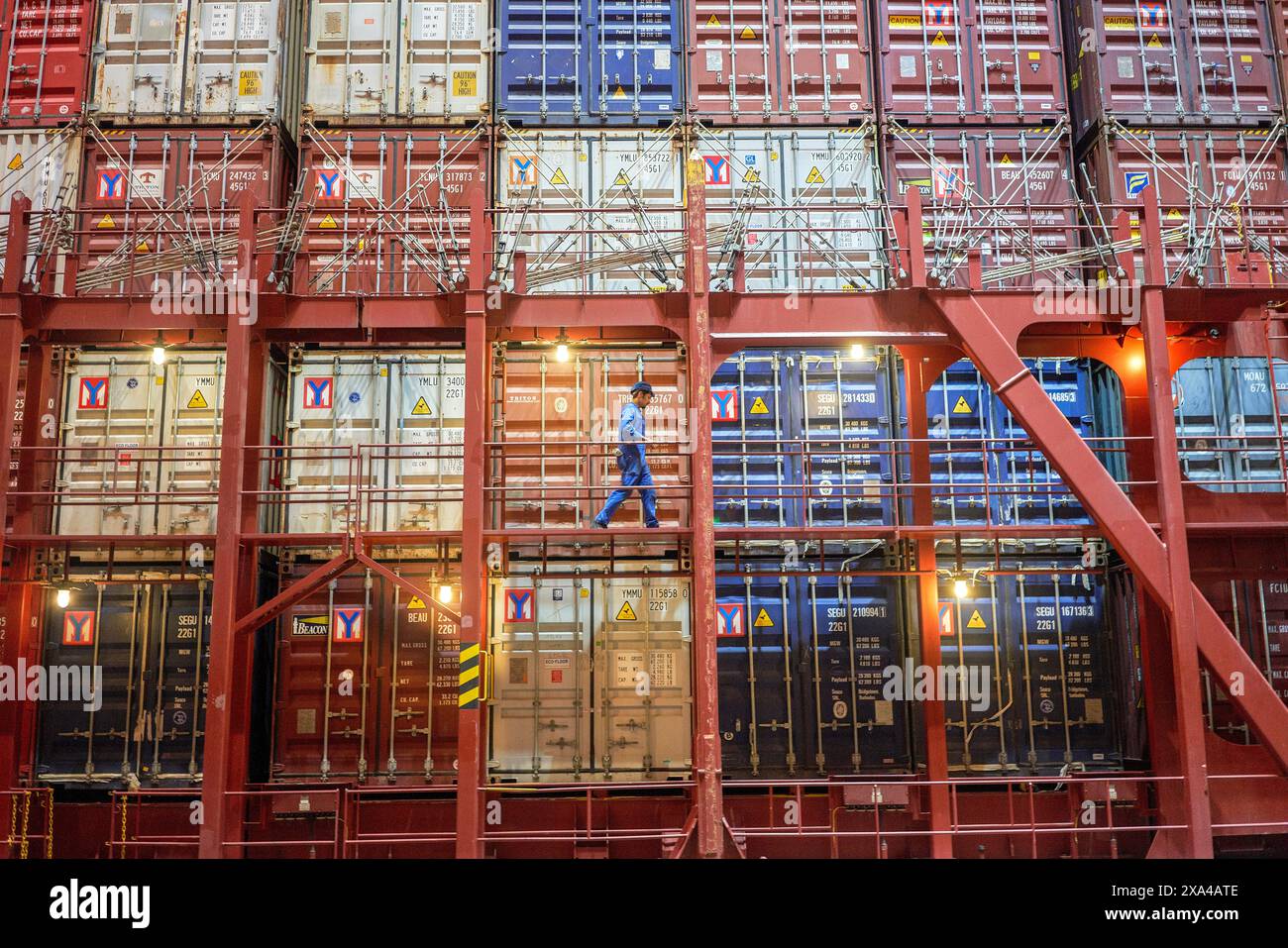 Un travailleur marche le long de la passerelle étroite d'un grand cargo, entouré de nombreux conteneurs empilés colorés. Banque D'Images