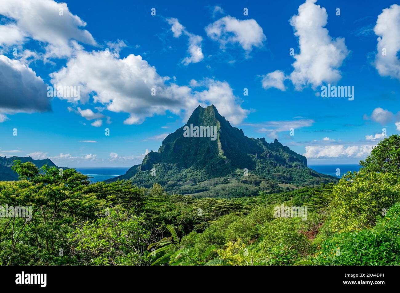 Un paysage saisissant avec un sommet de montagne vert luxuriant sous un ciel bleu parsemé de nuages blancs. Banque D'Images