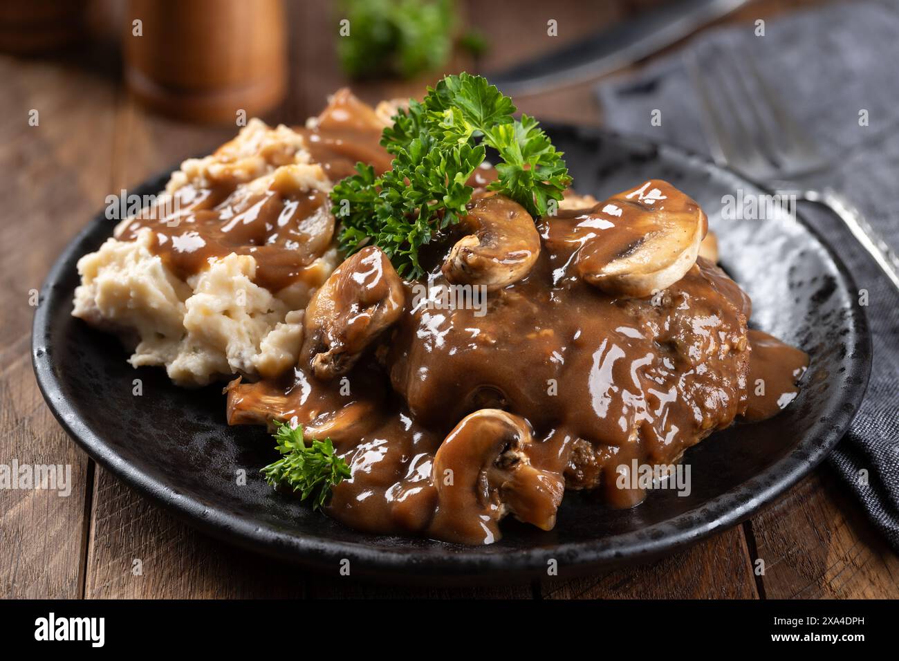 Steak Salisbury avec sauce aux champignons garnie de persil et de purée de pommes de terre sur une assiette noire Banque D'Images