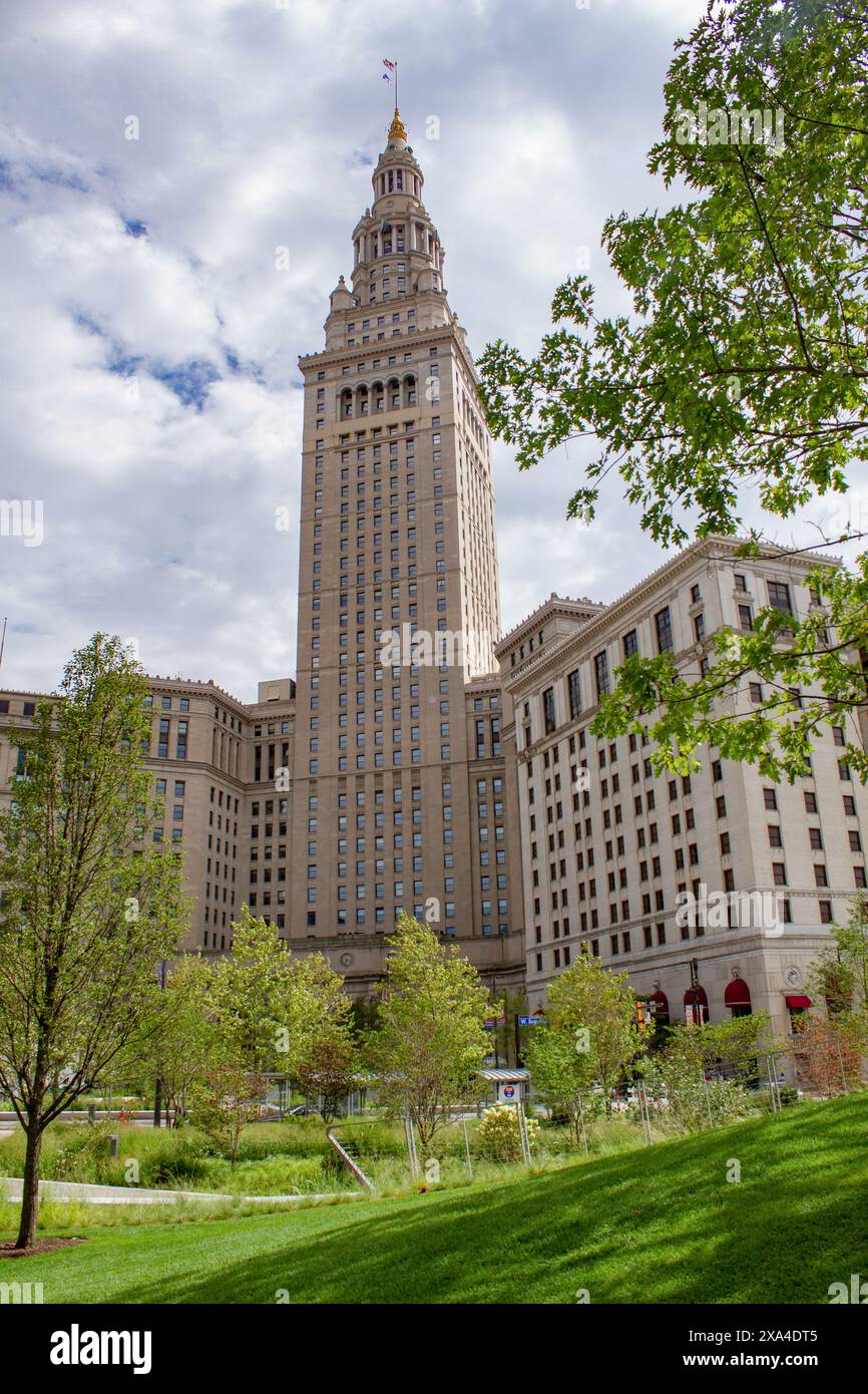 L'image montre un grand bâtiment historique avec une tour proéminente, sur fond de ciel partiellement nuageux et encadré par des arbres verdoyants au premier plan. Banque D'Images