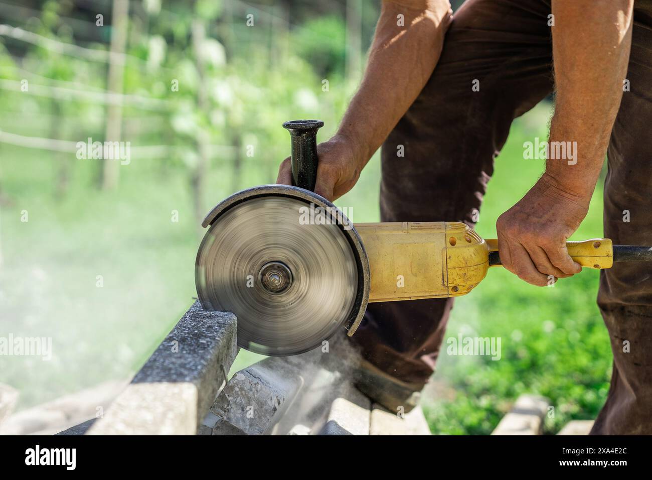 Personne utilisant un grand broyeur jaune pour couper des poteaux en béton dans le jardin de la maison. Disque diamanté en métal tournant pour couper le béton, lame rotative visible. Poussière et de Banque D'Images