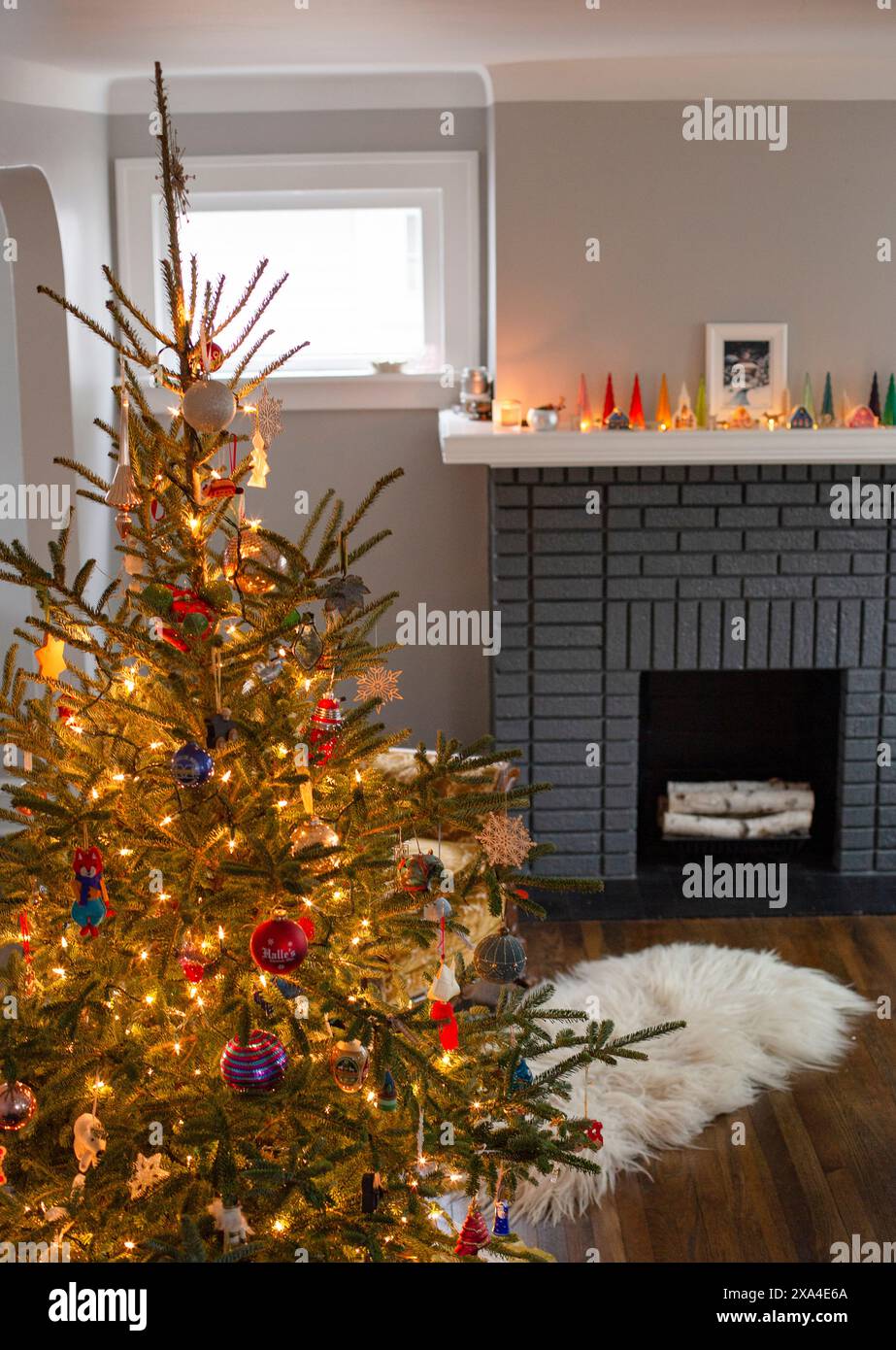 Un sapin de Noël bien décoré se dresse dans une pièce confortable avec une cheminée allumée et une série de bougies allumées sur la cheminée. Banque D'Images