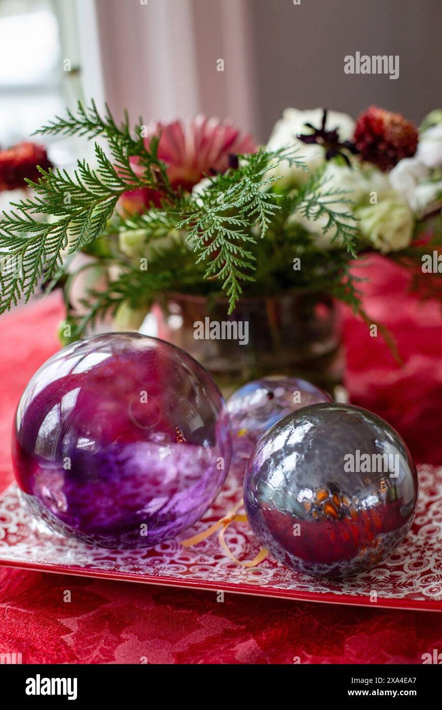 Une table vibrante et festive avec deux sphères décoratives réfléchissantes reposant sur un chemin de table en dentelle écarlate, accompagnées d'une composition florale luxuriante et de feuillages verts. Banque D'Images