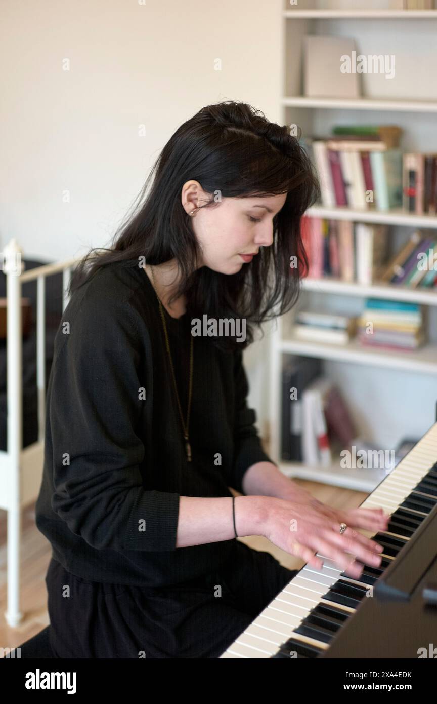 Une femme se concentre en jouant du piano dans une pièce avec une étagère en arrière-plan. Banque D'Images