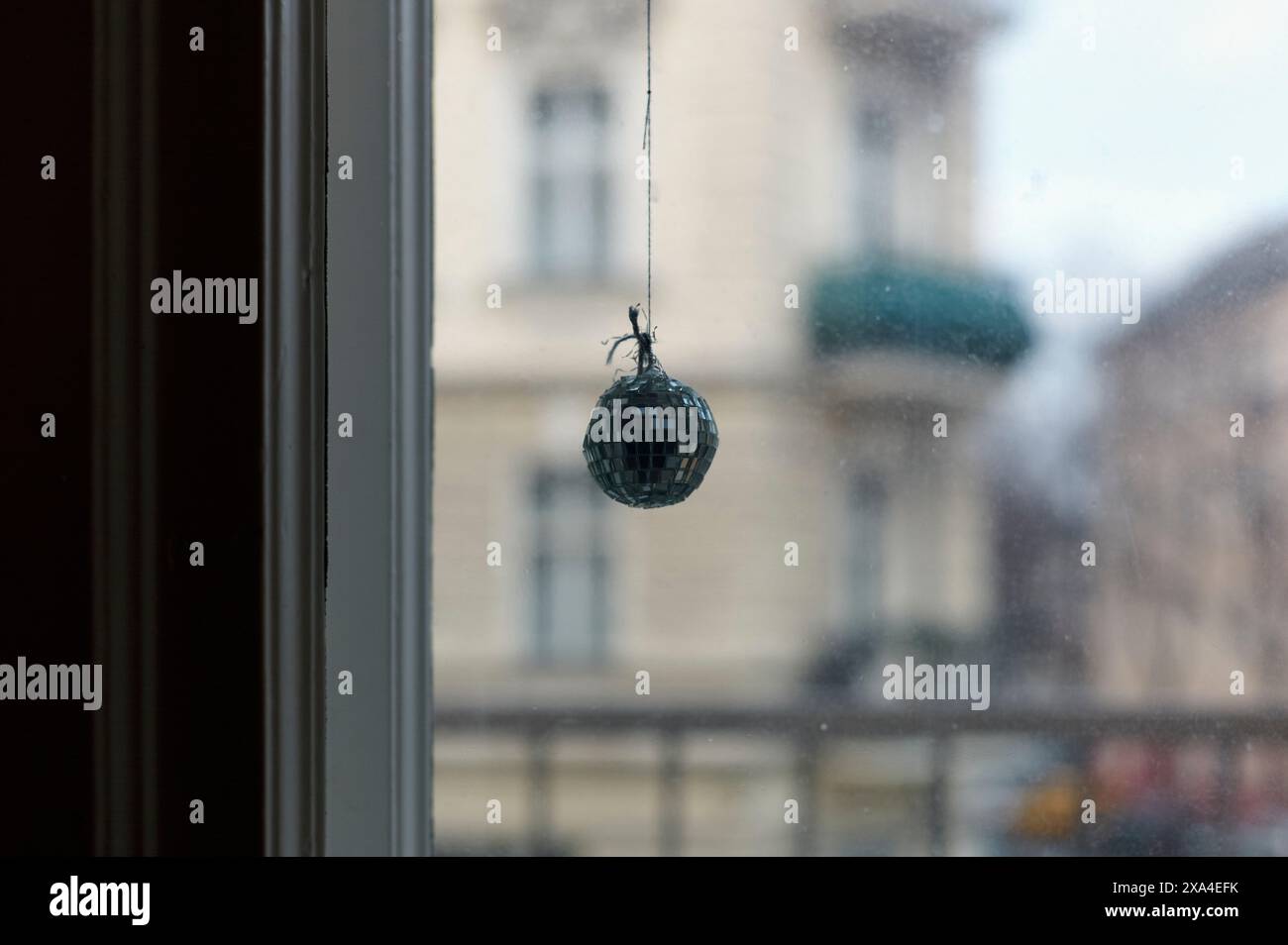 Une araignée est sur une petite boule disco suspendue par un fil devant une fenêtre avec des bâtiments visibles en arrière-plan. Banque D'Images