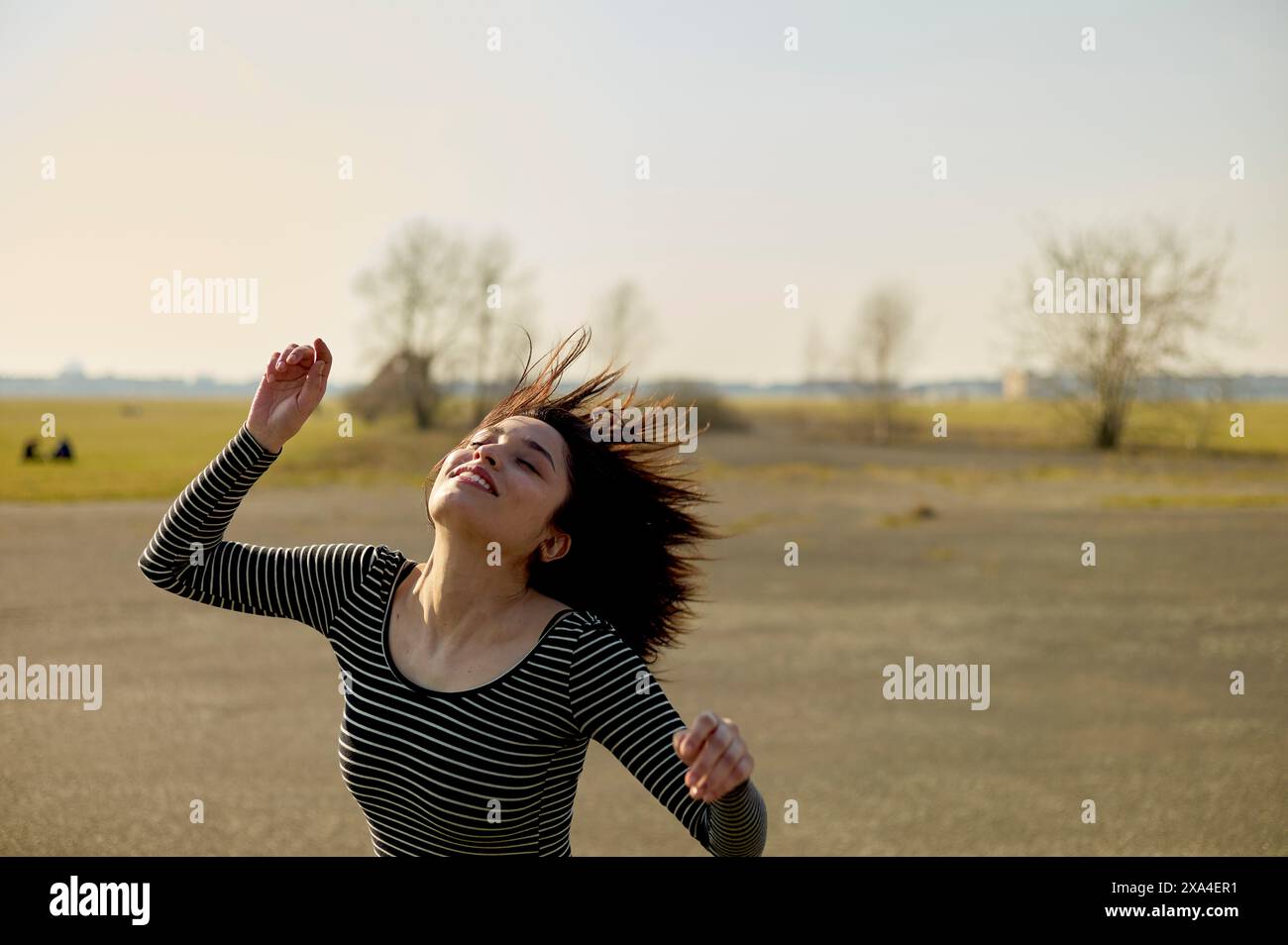 Une jeune femme joyeuse tourne avec ses cheveux coulant dans l'air par une journée ensoleillée avec un ciel dégagé et un champ ouvert en arrière-plan. Banque D'Images