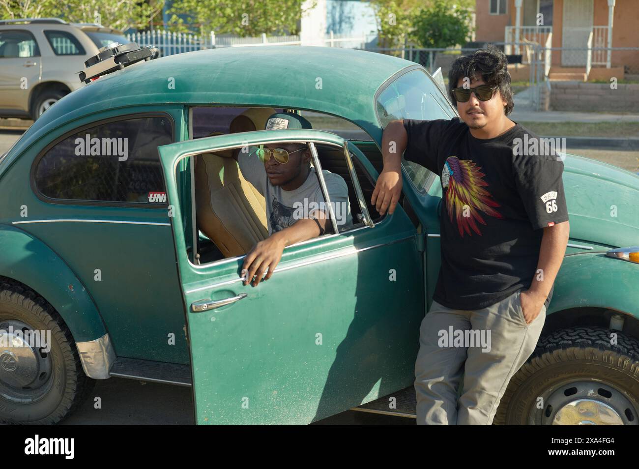 Deux jeunes hommes se tiennent debout à côté d'une Volkswagen Coccinelle verte vintage, l'un assis à l'intérieur avec la porte ouverte et l'autre appuyé sur la porte de l'extérieur. Banque D'Images