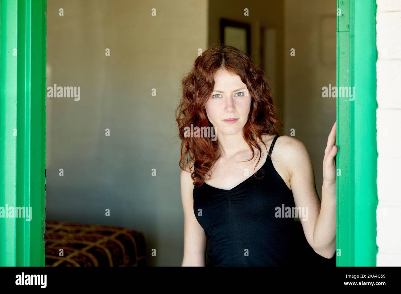 Une femme aux cheveux roux bouclés se tient dans une porte, portant un débardeur noir et donnant un look concentré. Banque D'Images