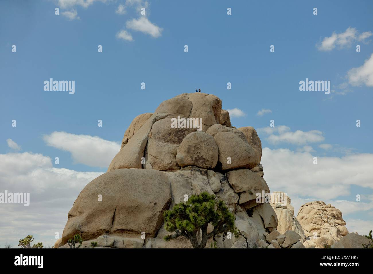 Un petit groupe de personnes se dresse au sommet d'une grande formation rocheuse de granit sous un ciel bleu nuageux. Banque D'Images
