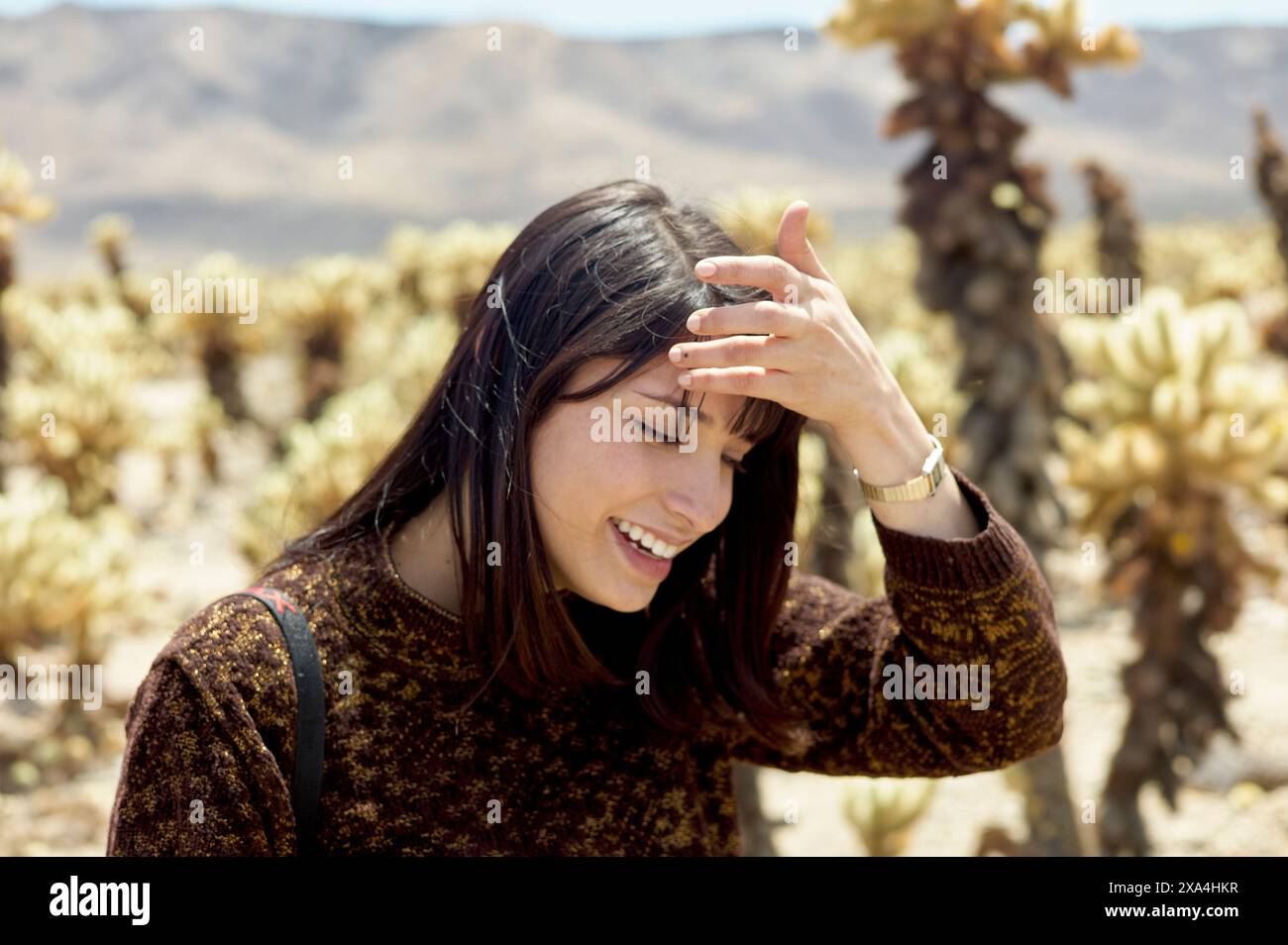Une jeune femme sourit dehors avec sa main sur son front, entourée de cactus sous un ciel ensoleillé. Banque D'Images Une jeune femme sourit dehors avec sa main sur son front, entourée de cactus sous un ciel ensoleillé. Banque D'Images