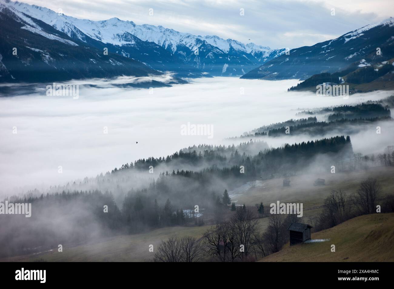 Un paysage montagneux brumeux avec des couches de brouillard installées dans les vallées, une petite cabane au premier plan et des sommets enneigés en arrière-plan. Banque D'Images