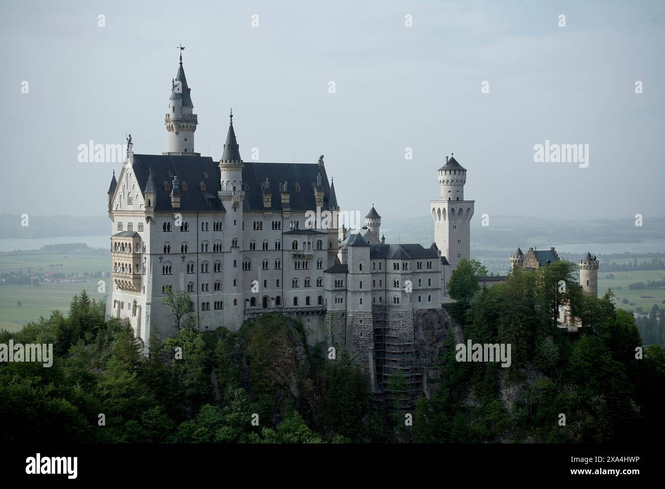 Majestueux château perché sur une colline luxuriante entourée de verdure et d'un lac lointain, sous un ciel brumeux. Banque D'Images