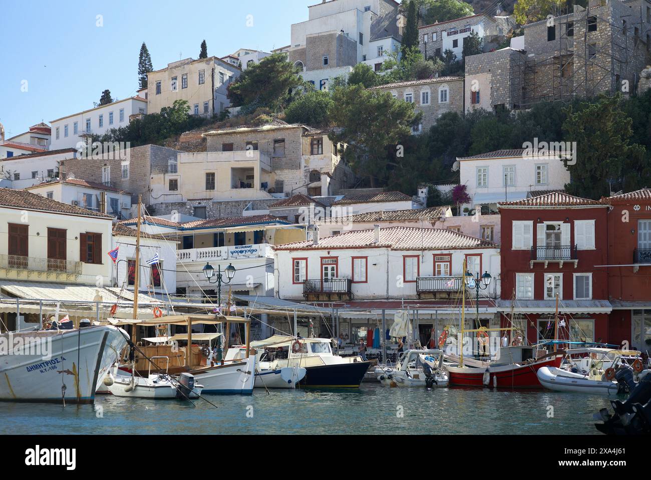 L'image montre une scène pittoresque d'une ville côtière avec des bateaux amarrés dans le port, des bâtiments traditionnels grimpant une colline, et un ciel bleu clair. Banque D'Images