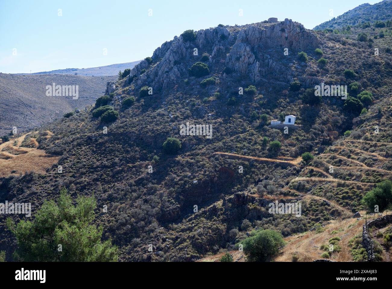 Un petit bâtiment blanc niché sur une colline avec un terrain accidenté couvert de végétation clairsemée sous un ciel bleu clair. Banque D'Images