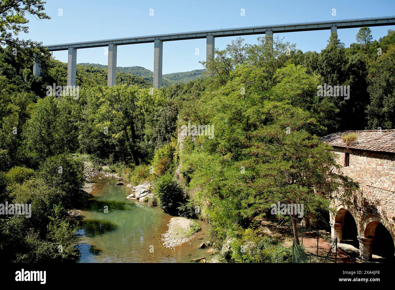 Un pont imposant s'étend à travers une vallée luxuriante et verdoyante avec une rivière qui coule en dessous, près d'un vieux bâtiment en pierre avec des arches. Banque D'Images