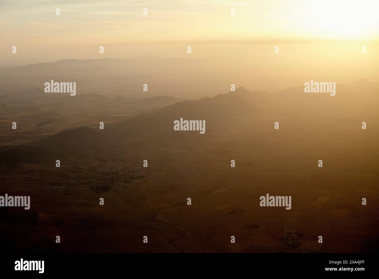 Vue aérienne d'un paysage montagneux baigné dans la lueur chaude du coucher ou du soleil levant, avec une brume diffusant la lumière du soleil. Banque D'Images