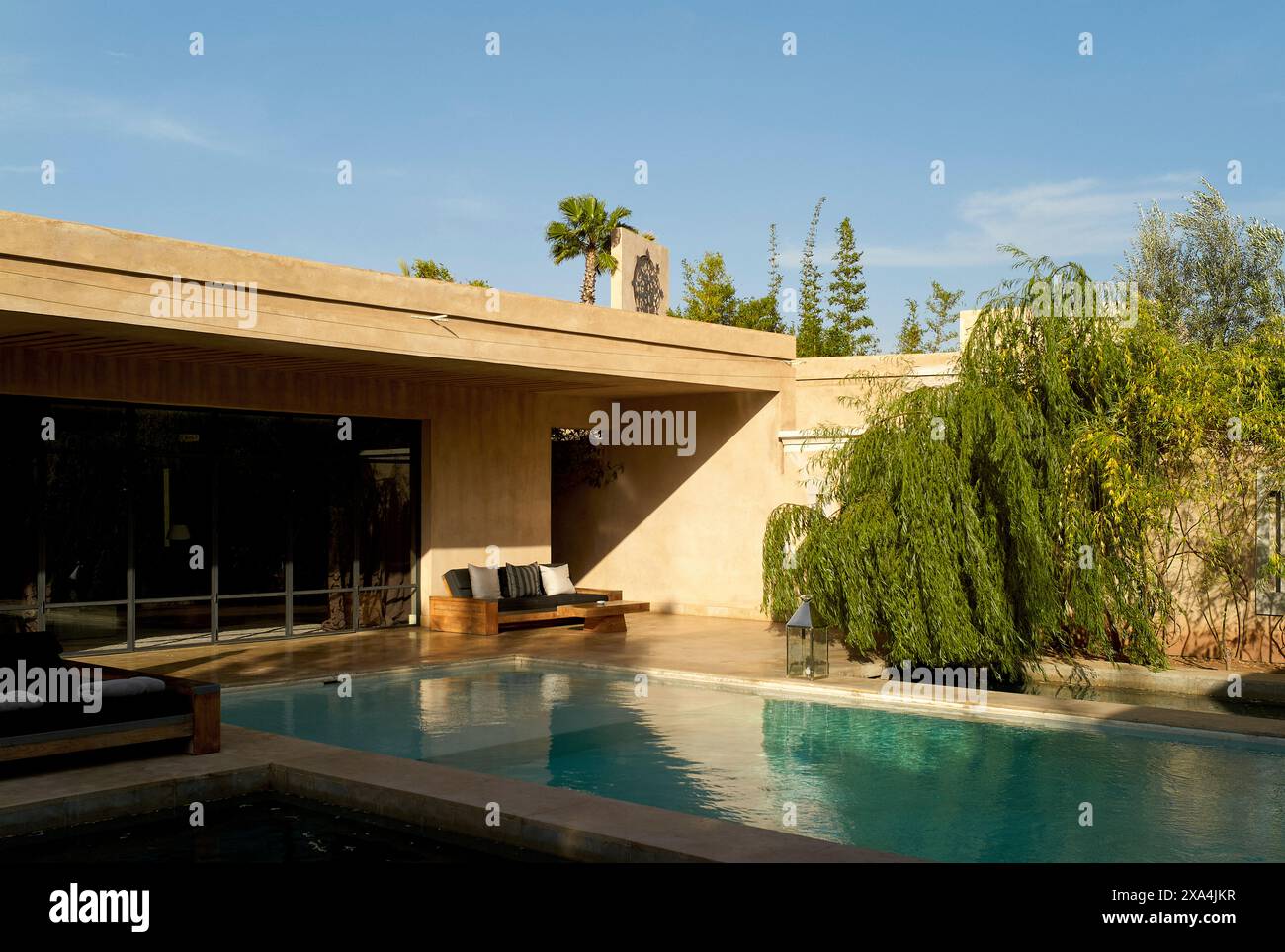 L'image montre une maison moderne avec une piscine extérieure entourée d'une végétation luxuriante et d'un ciel bleu clair. Banque D'Images