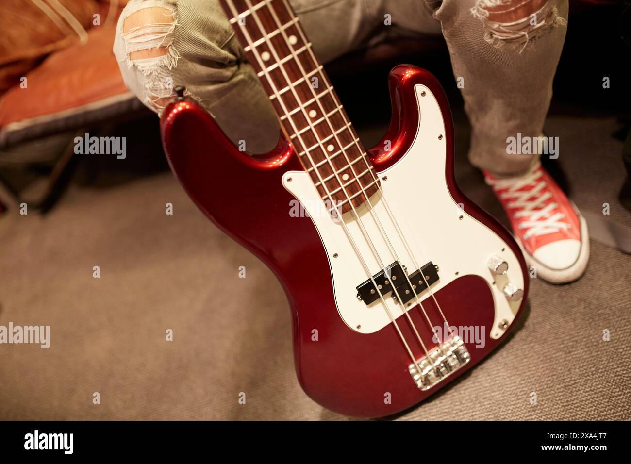 Une vue rapprochée d'une guitare basse électrique rouge appuyée contre quelqu'un portant un Jean denim et des baskets rouges. Banque D'Images
